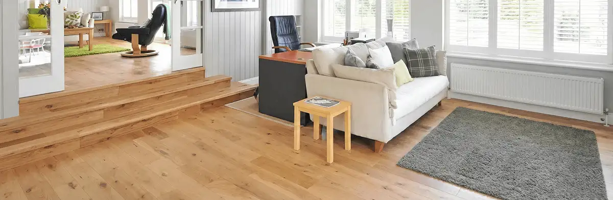 A modern living room with professionally installed laminate flooring, a beige sofa, a small side table, a gray rug, and large windows with white shutters in Allentown, PA